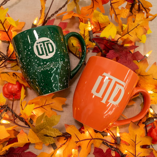 Two UT Dallas branded mugs along with fall foliage