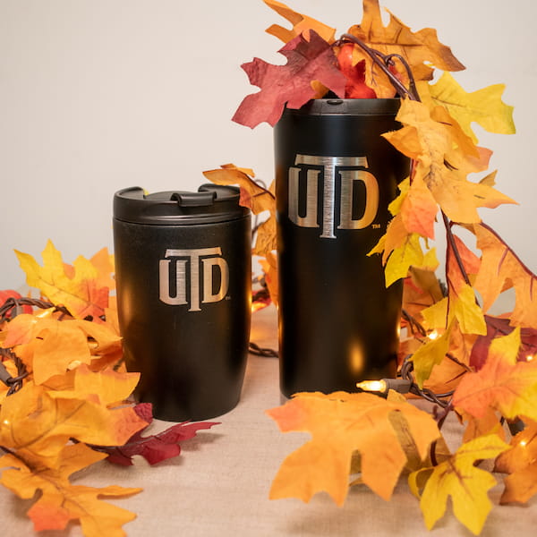 Two UTD branded tumblers, displayed among fall foliage.